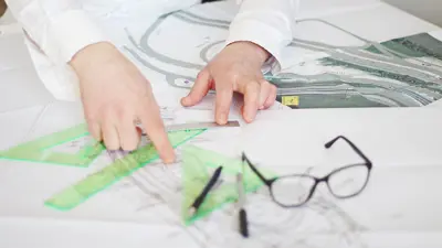 Person looking at plans on a table with glasses and pens on table