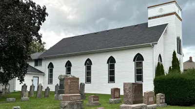 The exterior of the Niagara Falls Stamford Presbyterian Church. Showing some gravestones on green grass in the foreground and the white church building in the background.
