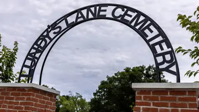 The Lundy's Lane Cemetery sign at the entrance. It is an arched black iron sigh with black lettering arching over the entrance, connected to brick support on each side.