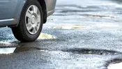 Close up of a car tire on a road with a waterfilled pothole.