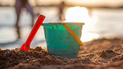 Kids pail and bucket on the shoreline of a beach with people in the water in the background.