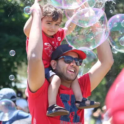 A man holding a child on his shoulders with soap bubbles in the air. They are enjoying the Canada Day celebration.