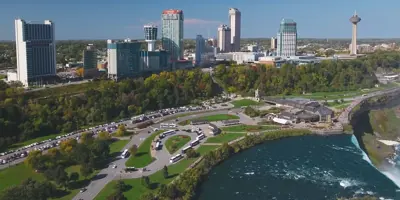 Image of the Niagara Falls in the summer with the horseshoe falls in the foreground and the city skyline and buildings in the background. 