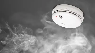 Image of a smoke alarm with grey smoke rising towards it.