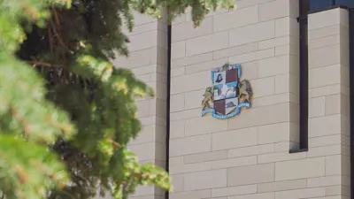 Exterior of City Hall showing the crest on the outside wall and a green tree in the foreground.