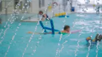 Swimming pool at MacBain Community Centre. Kids in background swimming with a blue pool noodles, water is spraying in the foreground.
