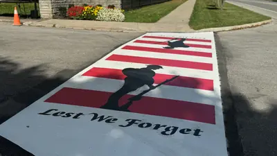 City of Niagara Falls Veterans crosswalk located at Fairview Cemetery.  It has red and white lines with black outline of soldier and "Lest We Forget" painted in black letters at one end.