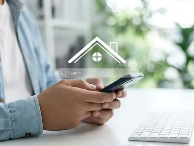 Person using smartphone with search bar overlay showing a house.