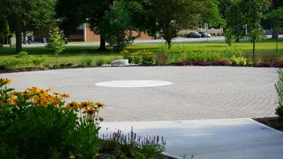 Circle paved area surrounded by gardens and flowers on the edging, with a path branching off from the centre.