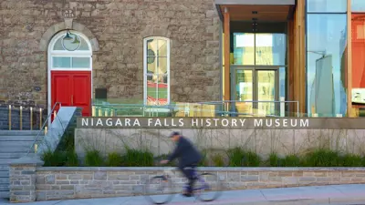 Exterior front of the Niagara Falls History Museum with a bright red front door.  An individual is going by on their bicycle.